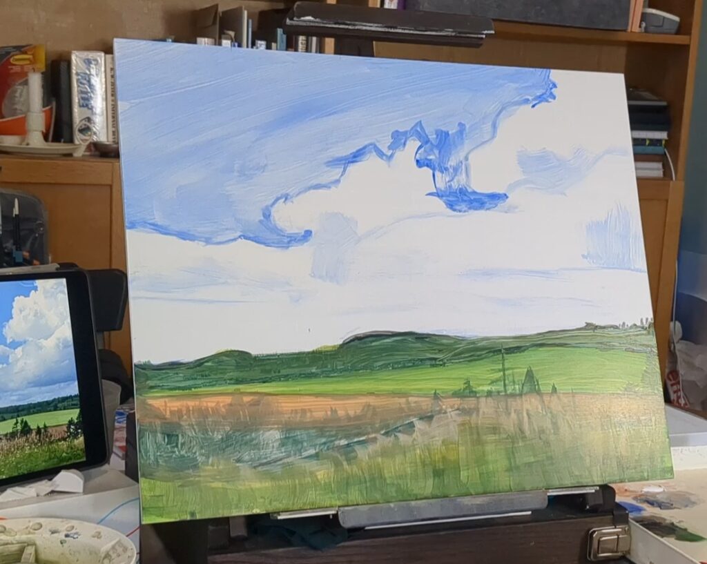 Painting in progress of rural landscape, shown on a table easel, between a tablet with reference photo on the left, a large palette on the right, and brushes in front.